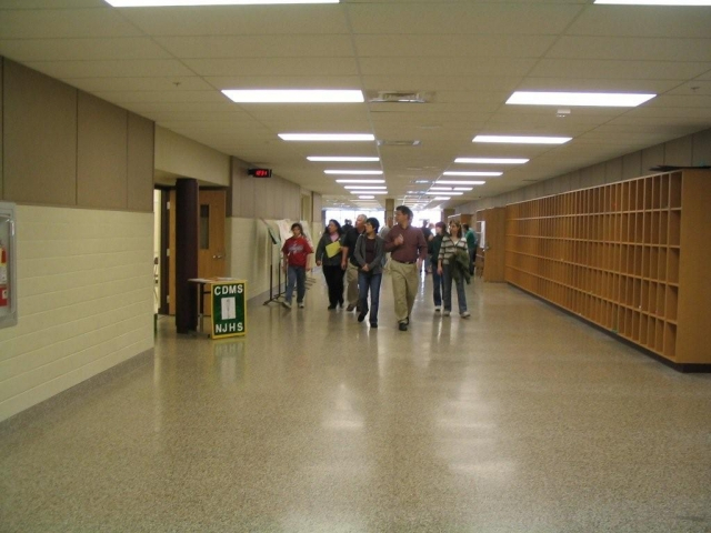 Looking down the hall into what used to be the cafeteria. Classrooms & lavs were built on the left side, cubbies on the right are where students store their books during lunch. The small auditorium is behind the wall of cubbies.