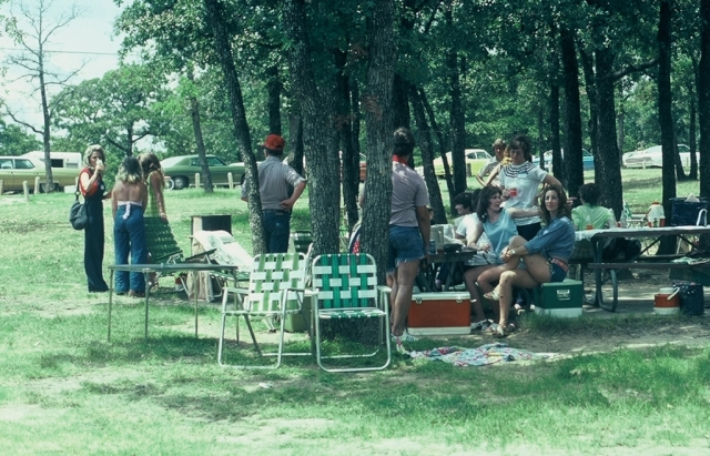 (034) 1975 Reunion Picnic Event:  Joy Bolman holding her leg, Gail Mackey pointing to something or someone, Gail Ince looking on.  Andy McGrady way in the back. Johnny Roland with his back to us.  That may be Durwood Williams to the left in the red baseba