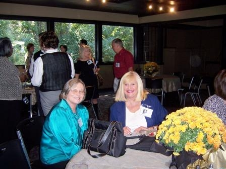 Kris Barnes and Debbie Drake sitting at the table. In the background, Anneita Cunningham, Beth Crocker, Ann McBride, Jimmy Hoppers