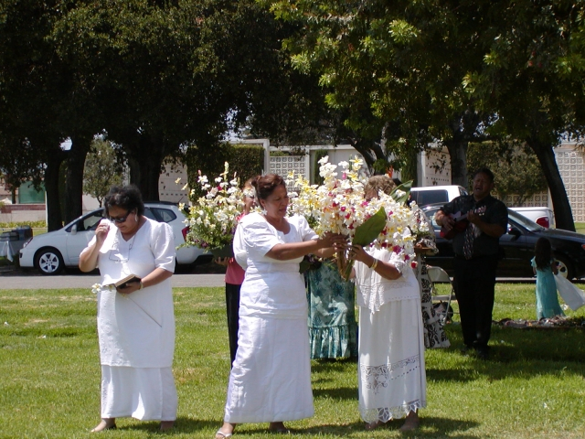 On the left, Lila (Levusis daughter) with the hymn book, Dorothy (Sanes daughter), center and Stella (Livas daughter) on the right arranging the floral arrangements to be placed on the graves of Salu, Alamoni and Kipeni. Sandy (Sanes son) is on the far ri